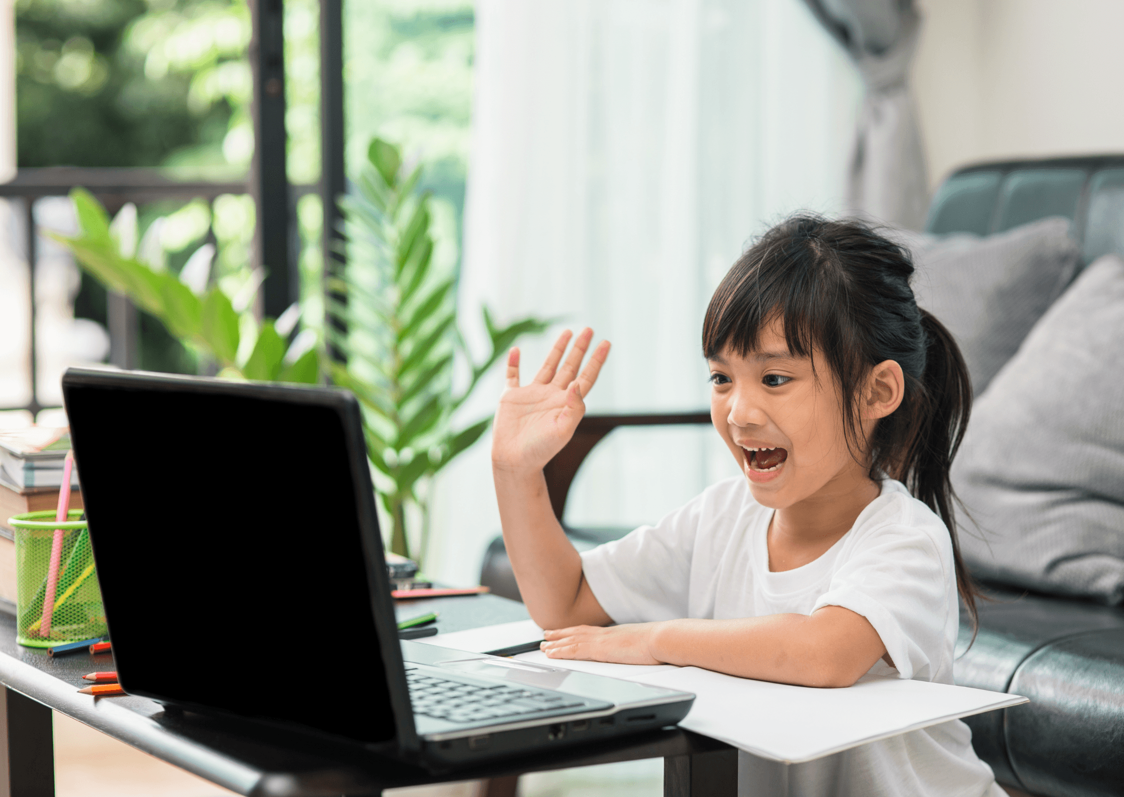 A young girl waving at her laptop at the start of a lesson