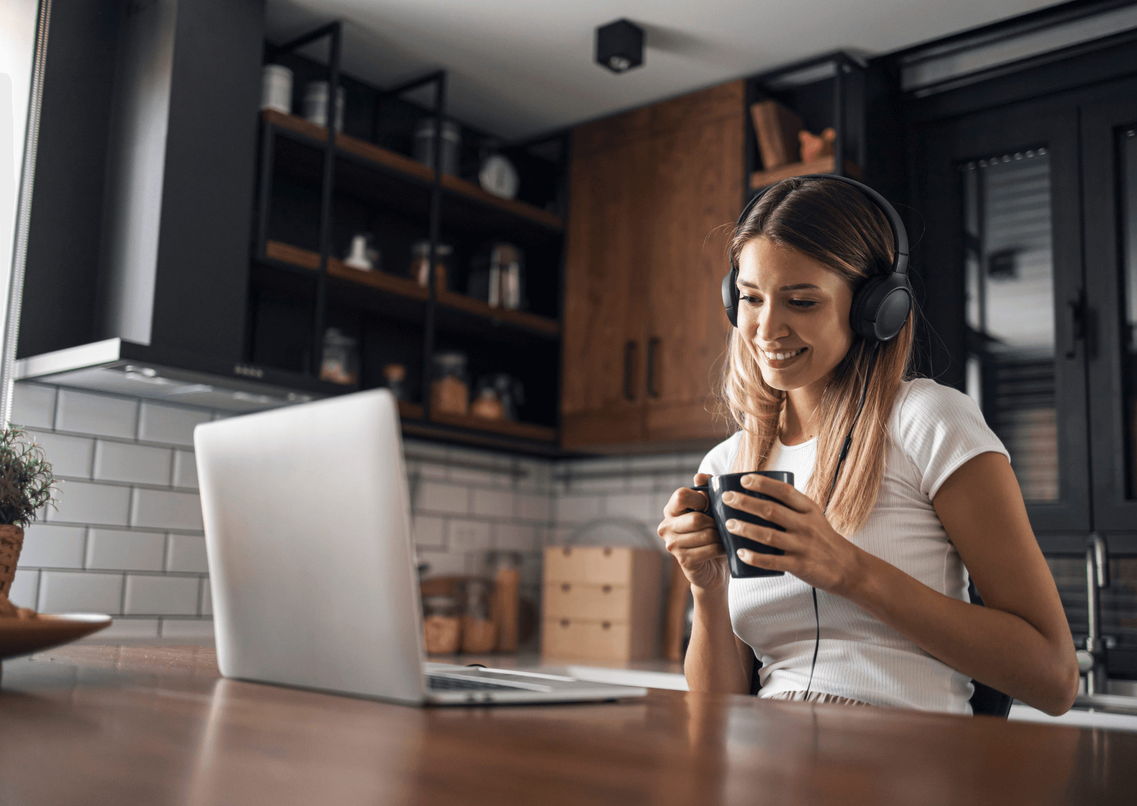 An adult learner with headphones and a mug, talking to her tutor from her kitchen